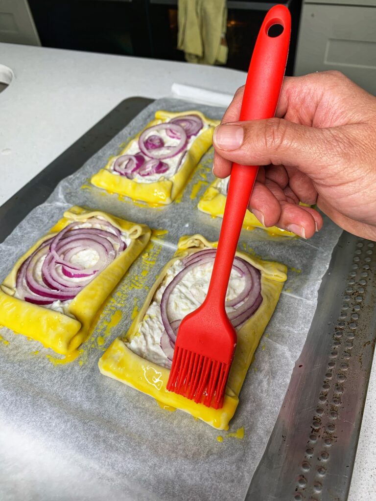 A hand is egg washing tartlets.