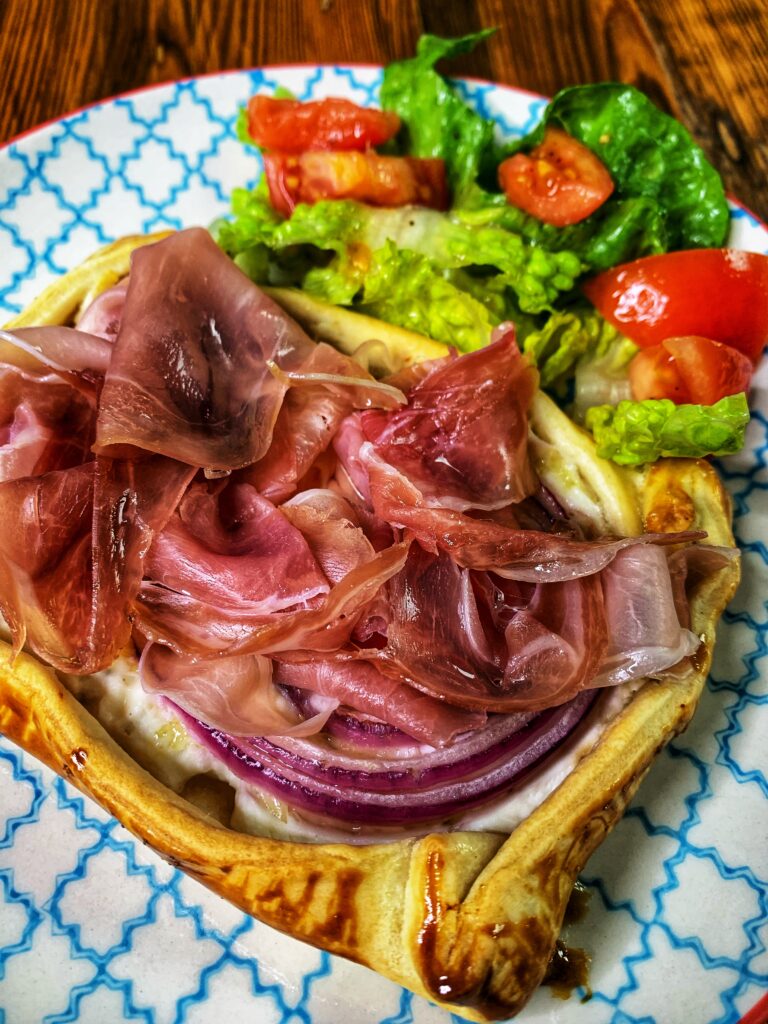 Prosciutto tart served in a plate with a side of lettuce and tomato salad.