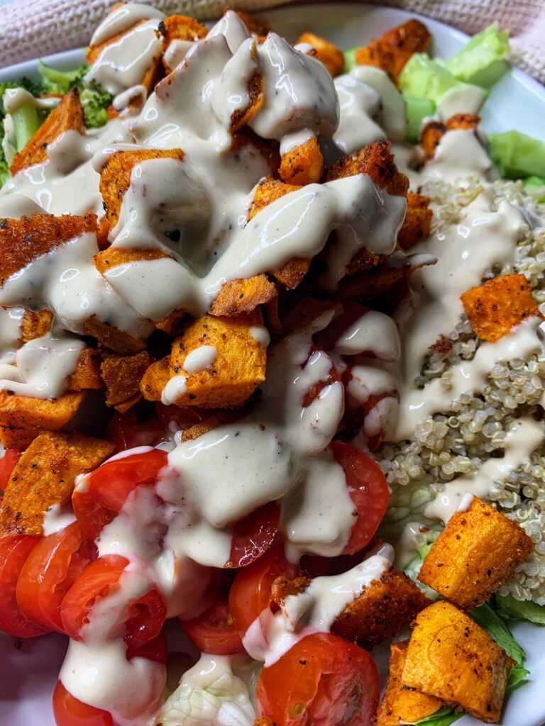 Roasted sweet potato salad serve on a plate with tomatoes, lettuce, quinoa, broccoli, and tahini dressing