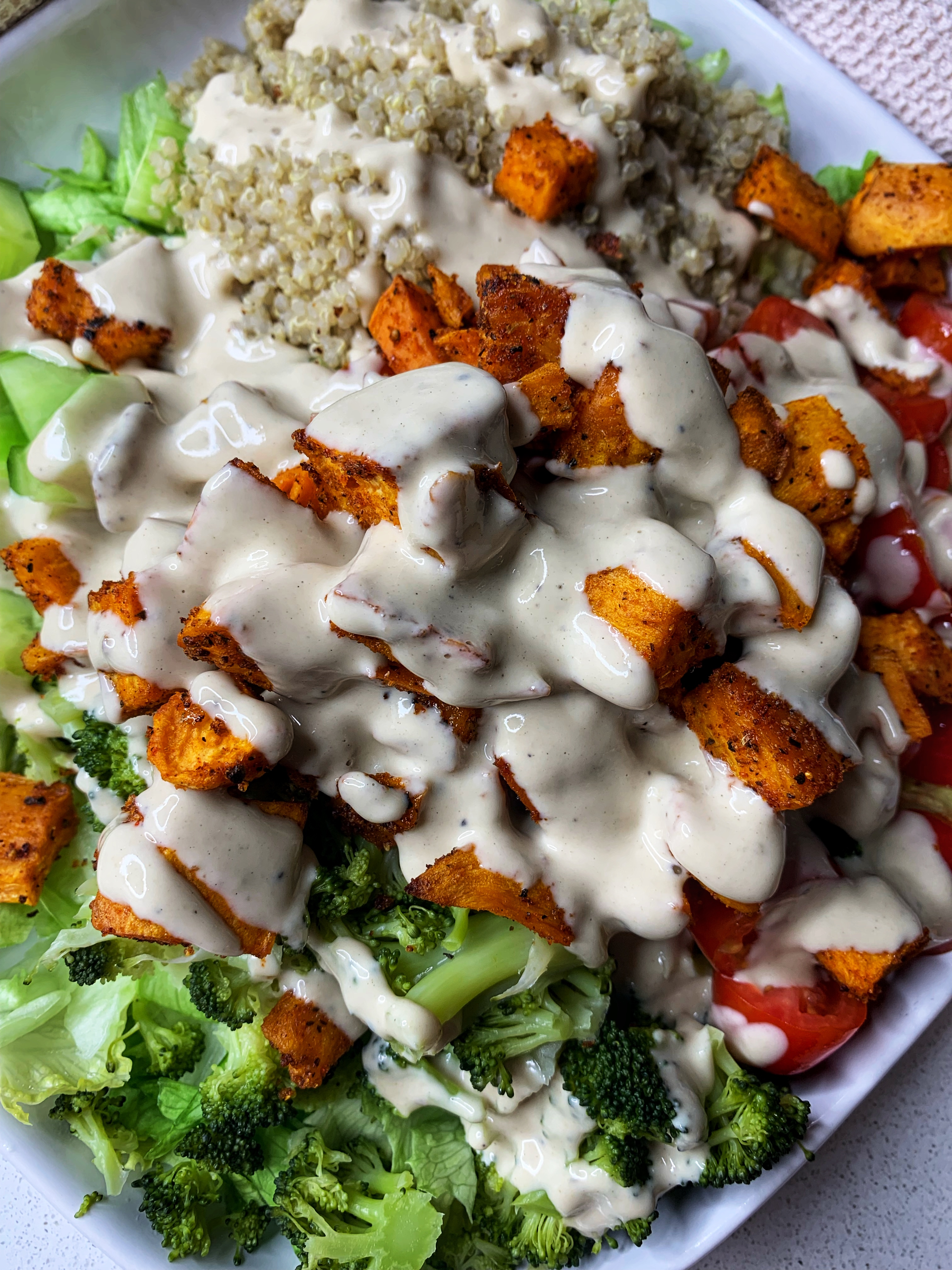 Roasted sweet potato salad serve on a plate with tomatoes, lettuce, quinoa, broccoli, and tahini dressing